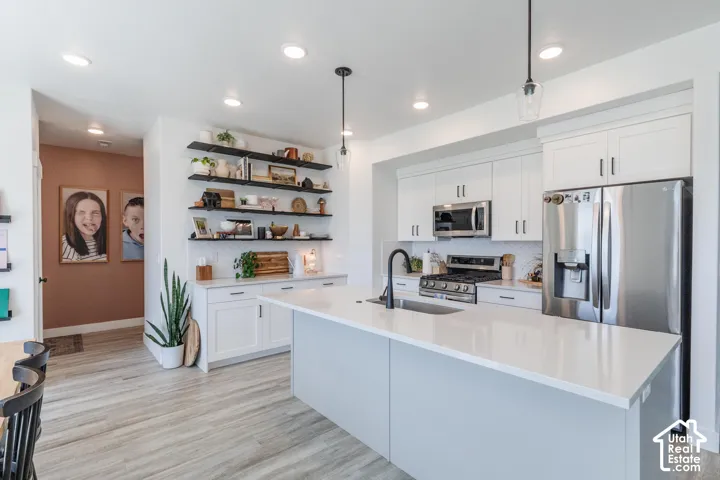 Kitchen with a central island featuring a sink, stainless steel appliances, white cabinetry, and open shelving
