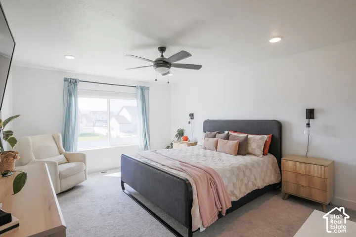 Recessed lighting, ceiling fan, expansive window, upholstered bed frame, and wall-mounted sconce lighting