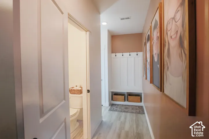 Recessed lighting illuminates the hallway with wood-finish flooring, featuring a built-in bench with storage and coat hooks