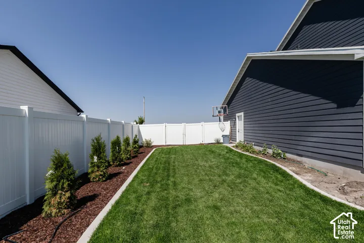 Expansive grassy yard with a concrete border, white privacy fencing, and wood chip landscaping with planted shrubs