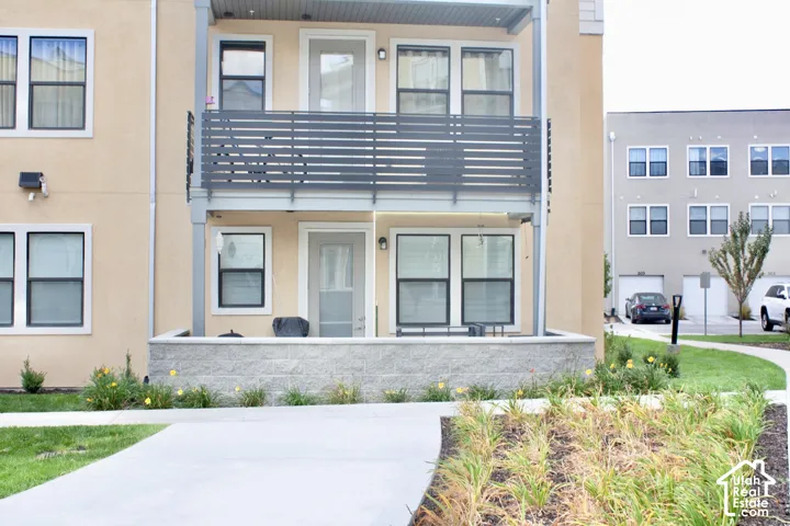 Stucco exterior with multiple windows, a ground-level patio, and an upper-level balcony featuring a metal railing