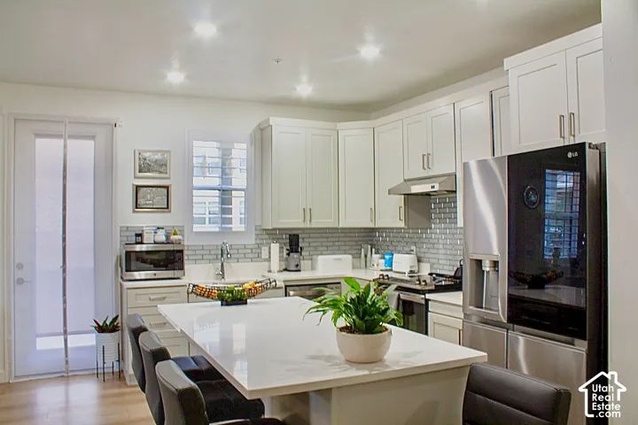 Spacious kitchen featuring an expansive island, light-toned cabinetry, stainless steel appliances, a subway tile backsplash, and wood-finish flooring