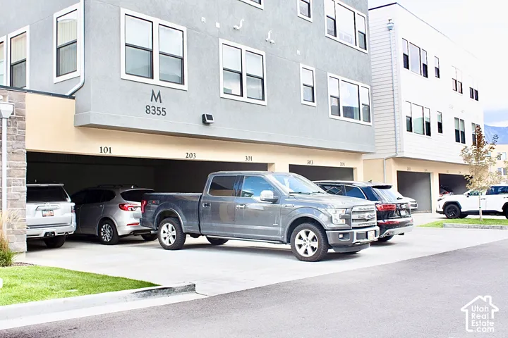 Multi-story building with gray and white siding, individual garage bays, and a concrete driveway