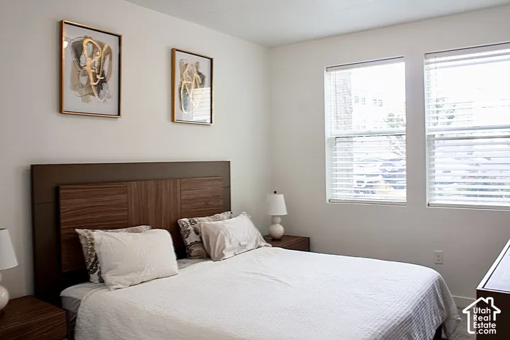 White wall finishes, two windows with blinds, and a wood-finish headboard