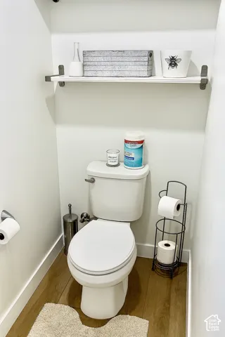 White wall-mounted shelving with exposed brackets, wood-finish flooring, and a white toilet