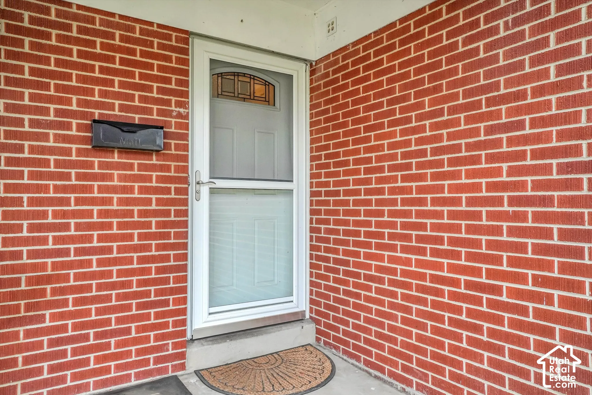 Red brick exterior with white trim, a white storm door, and a traditional mailbox