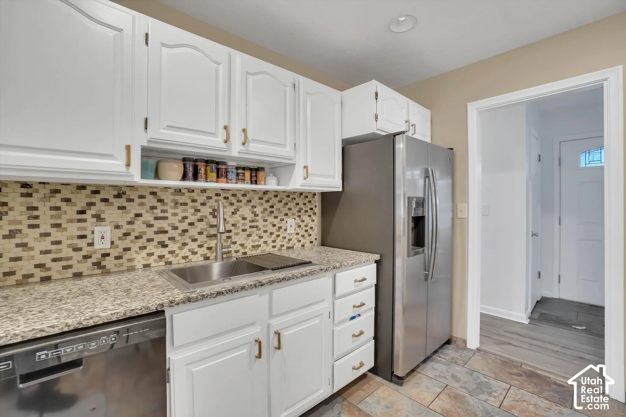 Kitchen featuring white cabinetry, a mosaic tile backsplash, a stainless steel sink, and granite countertops