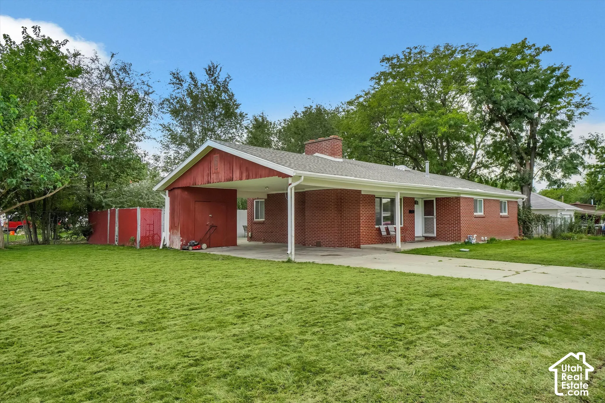 Brick exterior residence featuring a covered carport, attached red storage shed, and a paved driveway