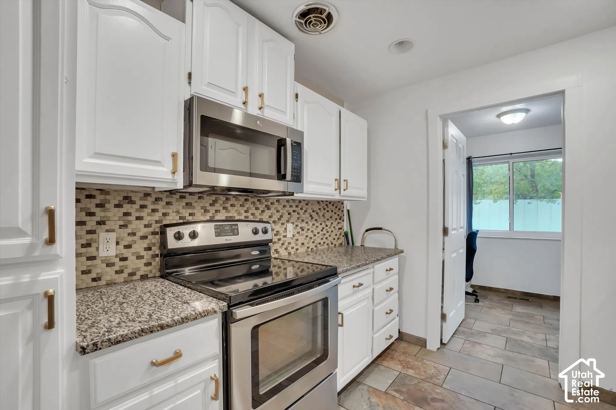 White cabinetry with brass-finish hardware, granite-look countertops, stainless steel appliances, and a mosaic tile backsplash