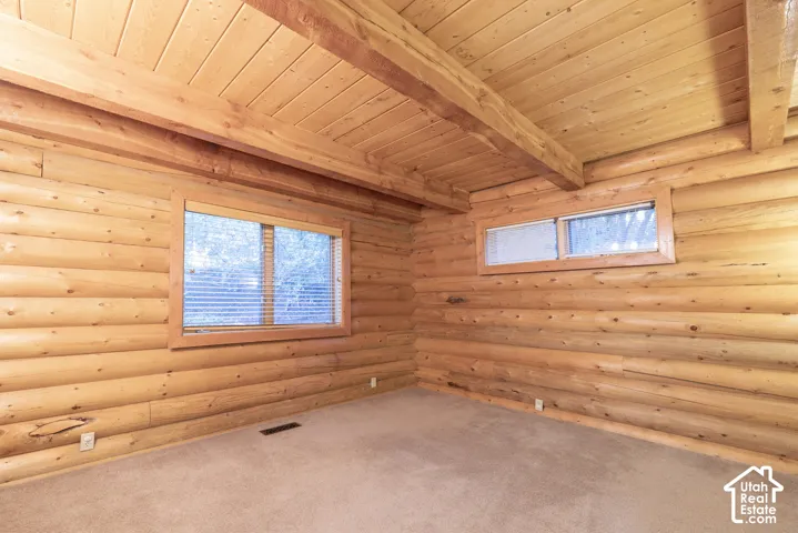 Wood-paneled ceiling with exposed beams, log wall construction, and two windows providing natural illumination