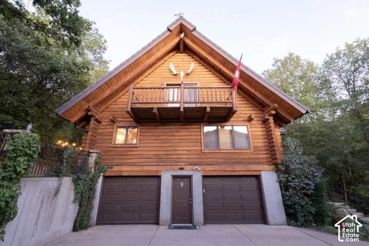 Log cabin exterior featuring a gable roofline, upper-level balcony, and two-car garage with brown doors