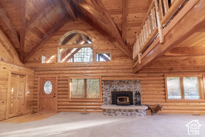 Expansive interior featuring log walls, exposed wood beams, a stone fireplace, and an arched transom window