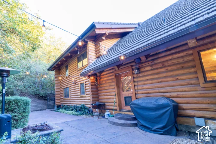 Log exterior home featuring a concrete patio, stone fire pit, and a retaining wall
