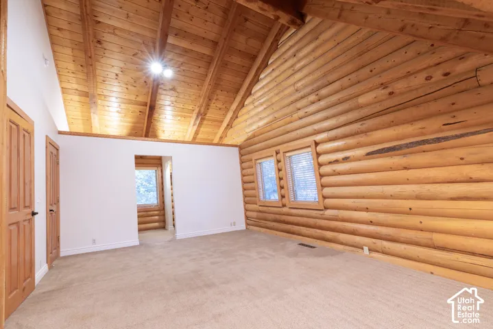 Exposed log wall construction, natural wood vaulted ceiling, light-toned carpeting, and multiple windows