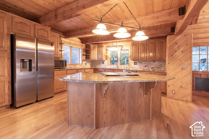 Kitchen featuring wood-paneled walls, wood-finish flooring, wood cabinetry, a granite-finish island, and stainless steel appliances