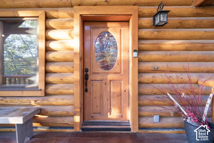 Log home exterior featuring a wood entry door with oval glass, a fixed window with wood trim, and a wall-mounted exterior light fixture