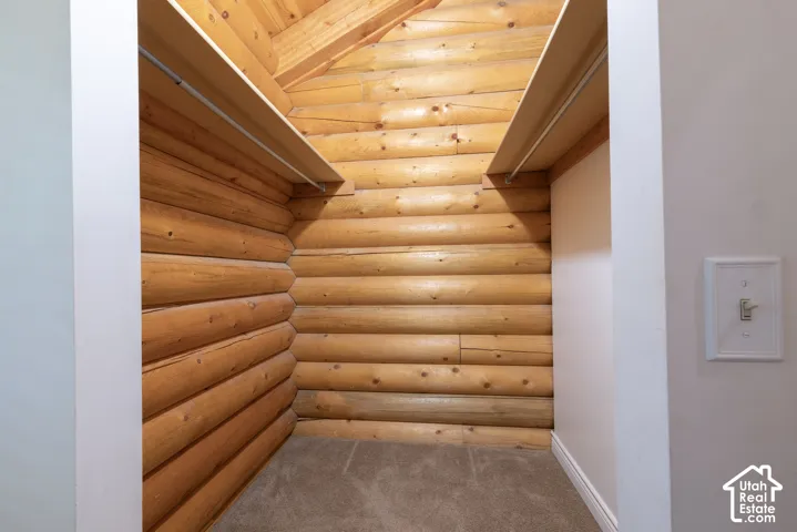 Log construction interior, sloped wood-paneled ceiling, two built-in shelves, and carpeted flooring