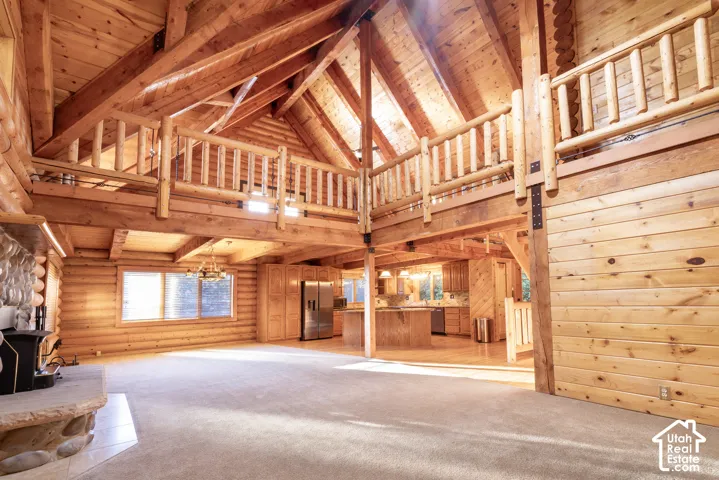 Vaulted timber ceilings, exposed wood beams, open loft area with wood railing, stone fireplace, and wood-finish flooring