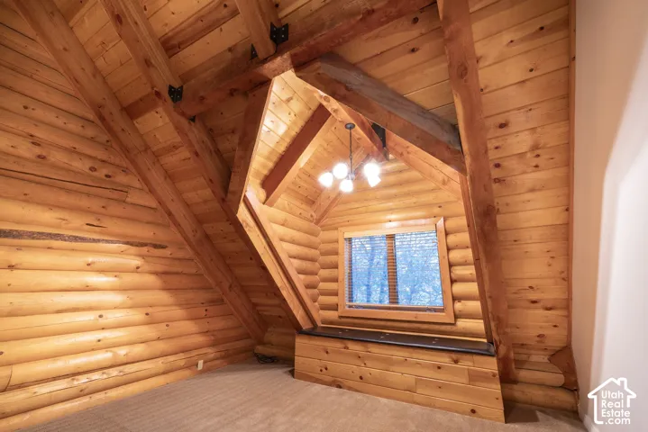 Cathedral ceiling with exposed wood beams, log wall construction, built-in window seat, and central chandelier