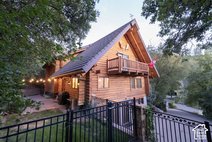 Log-style exterior with a dark-pitched roof, a second-story wood balcony, multiple windows, and a stone-clad pillar