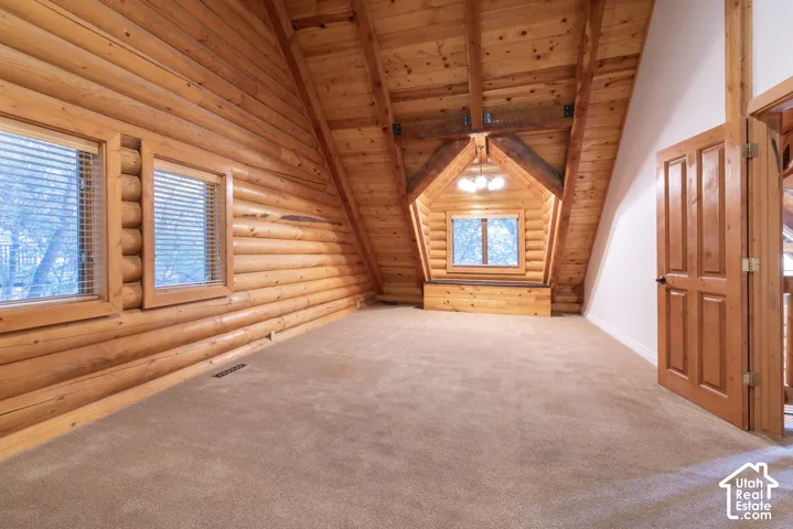 Exposed timber log walls, wood-paneled vaulted ceiling, built-in window seat, three-light chandelier, and carpet flooring