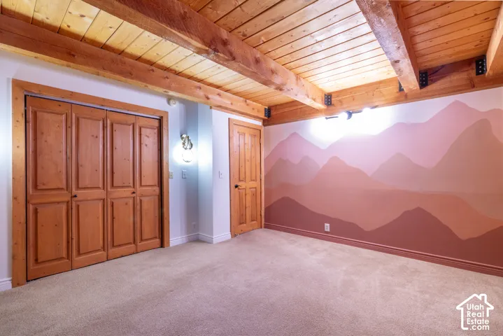 Exposed wood beam ceiling, wood plank ceiling, wood-paneled bifold closet doors, wood-paneled interior door, wall-mounted light fixture