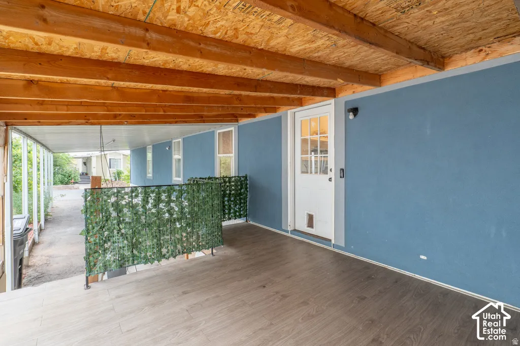 Covered outdoor space featuring wood-finish flooring, exposed wood beam ceiling, and a full-light entry door
