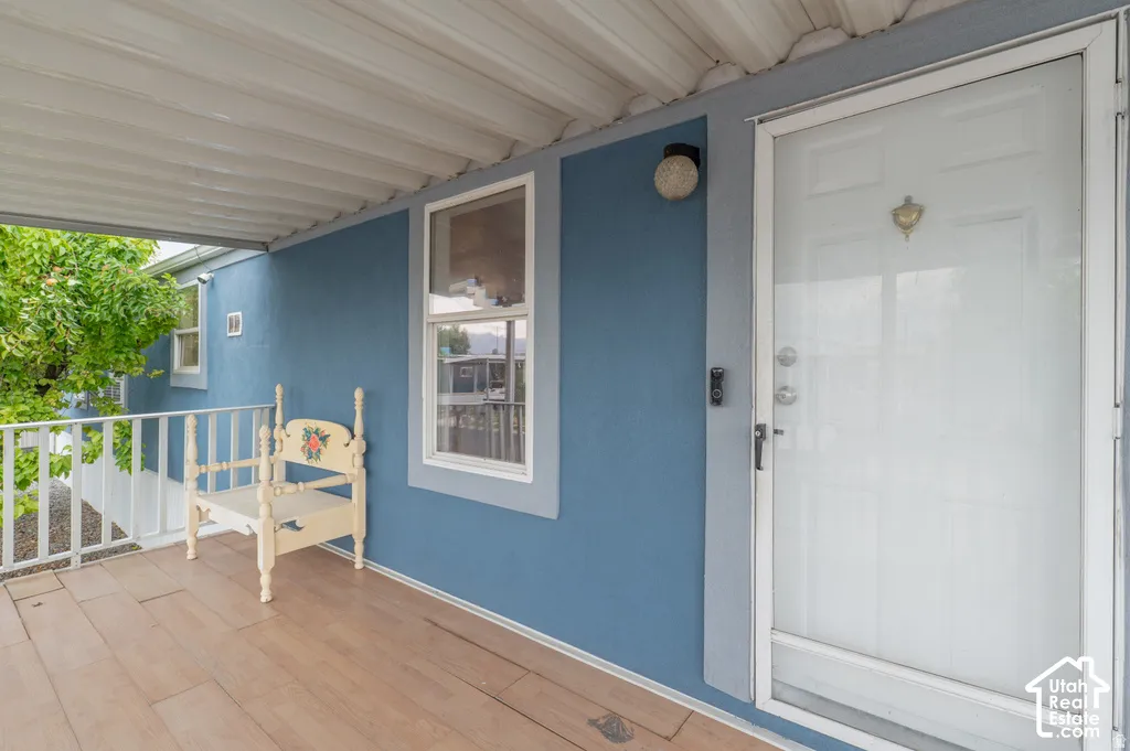 Covered porch with wood-finish flooring, white railing, and a storm door