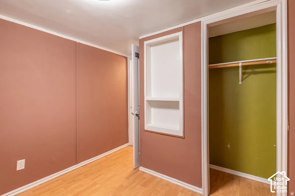 Wood-finish flooring with white trim, built-in shelving, and an integrated closet with a hanging rod