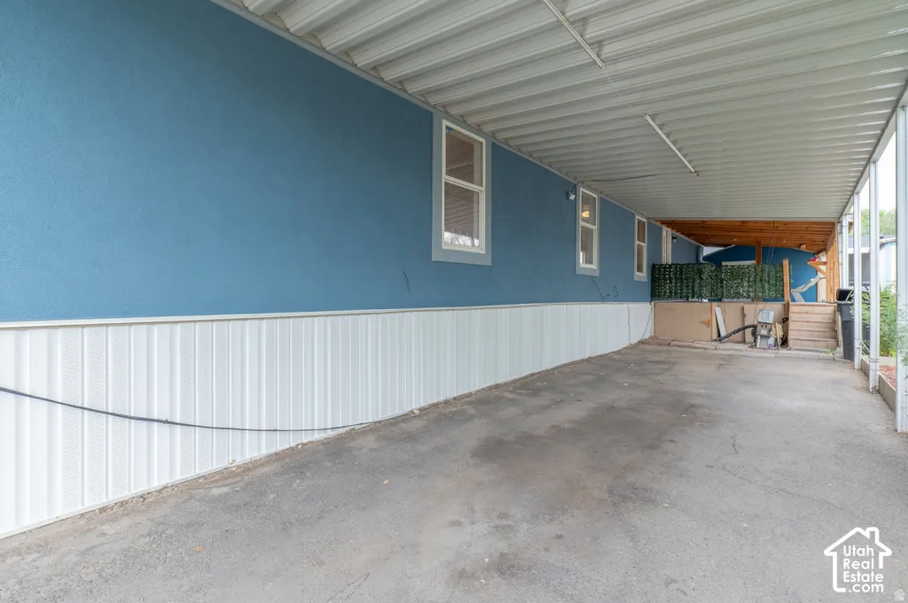 Covered parking structure with a corrugated metal roof, textured blue exterior wall, and white vertical paneling
