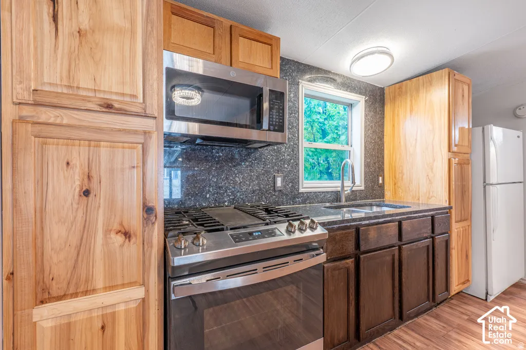 Stainless steel appliances, built-in microwave, gas range, dark cabinetry, and light wood-finish flooring