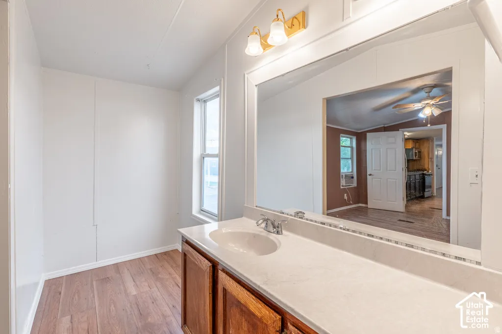 Wood-finish flooring with a single window and a vanity featuring a single basin sink, chrome faucet, and a large mirror