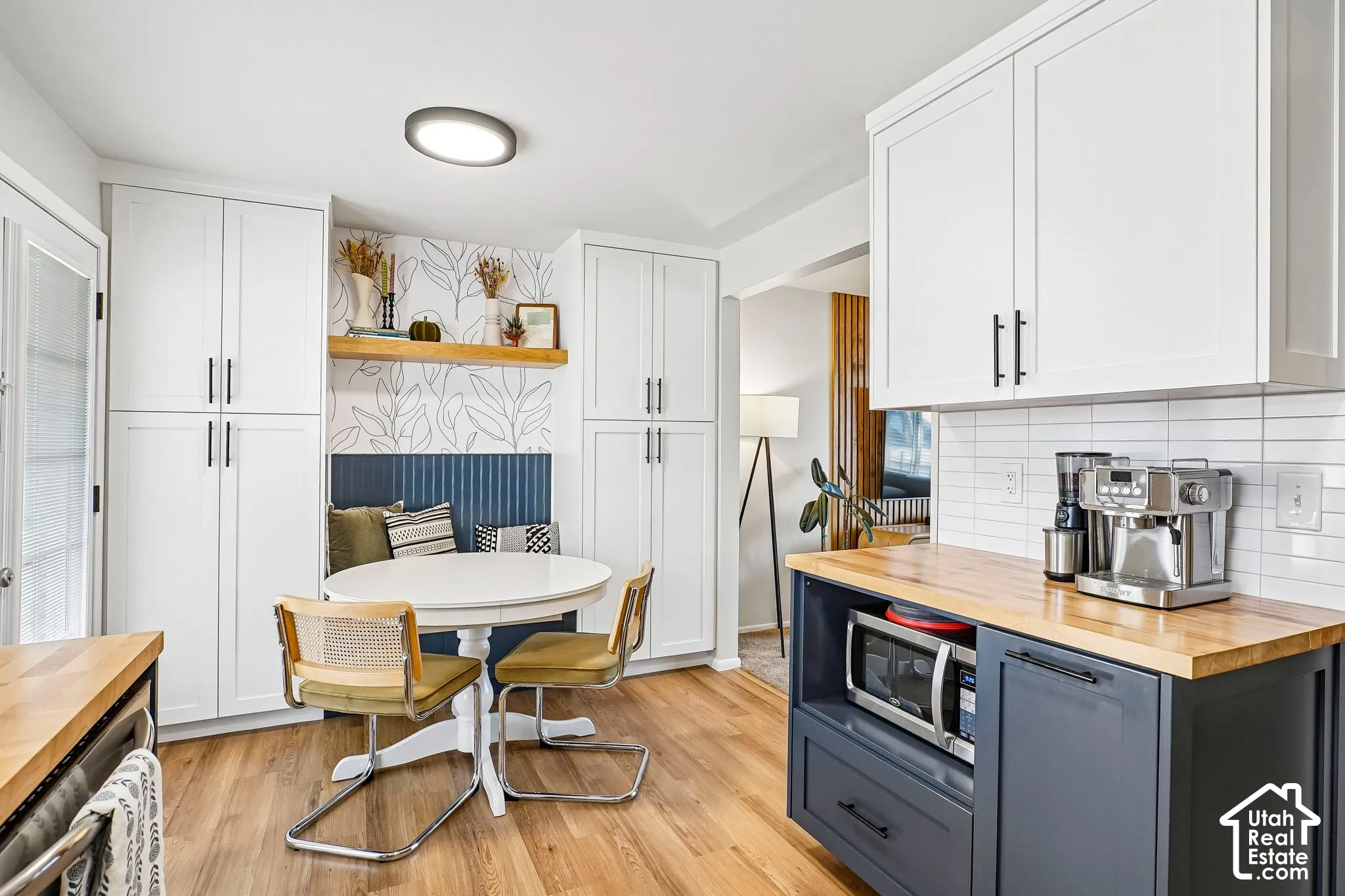 White cabinetry with matte black hardware, wood-finish flooring, white subway tile backsplash, built-in breakfast nook with floating wood shelf, and a kitchen island with a wood countertop