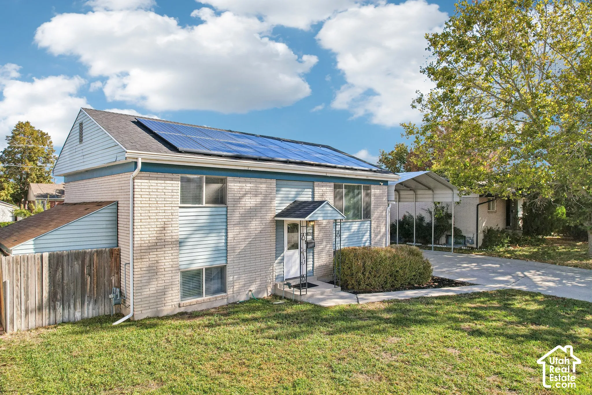 Split-level residence featuring a brick and siding exterior, solar panel installation, and a paved driveway with a covered carport