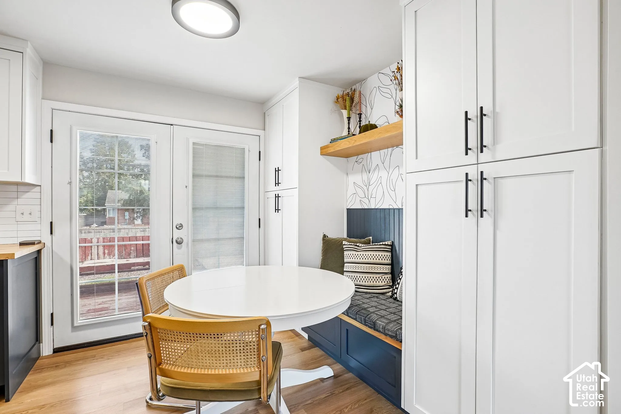 White shaker-style cabinetry with matte black hardware, built-in bench seating, wood-finish flooring, and white French-style patio doors