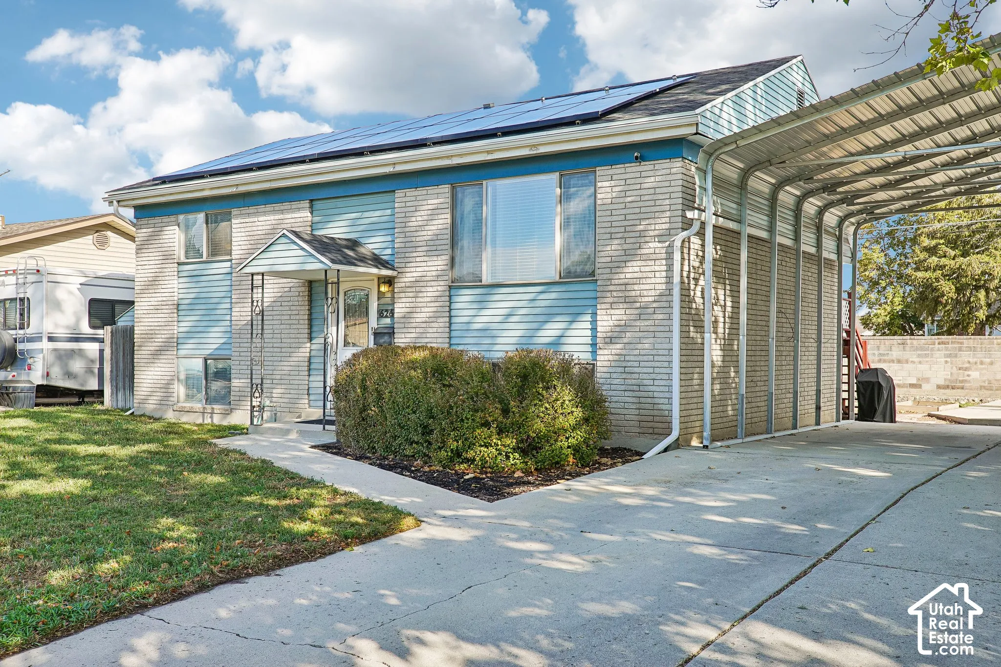 Brick and siding exterior with a covered entry, solar panels, a concrete driveway, and an attached carport