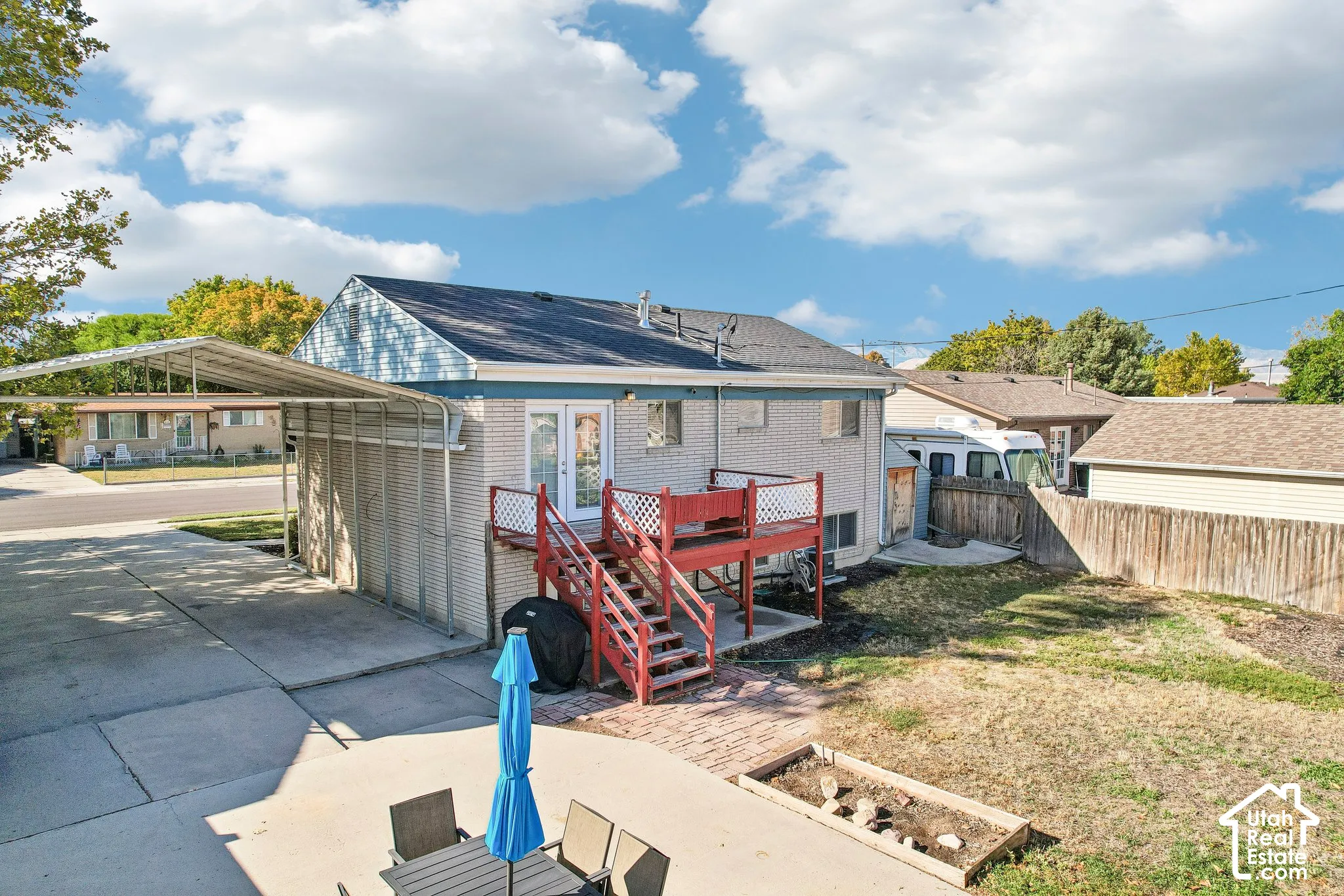 Rear exterior featuring a red-painted deck, an attached carport, a concrete driveway, and a fenced yard