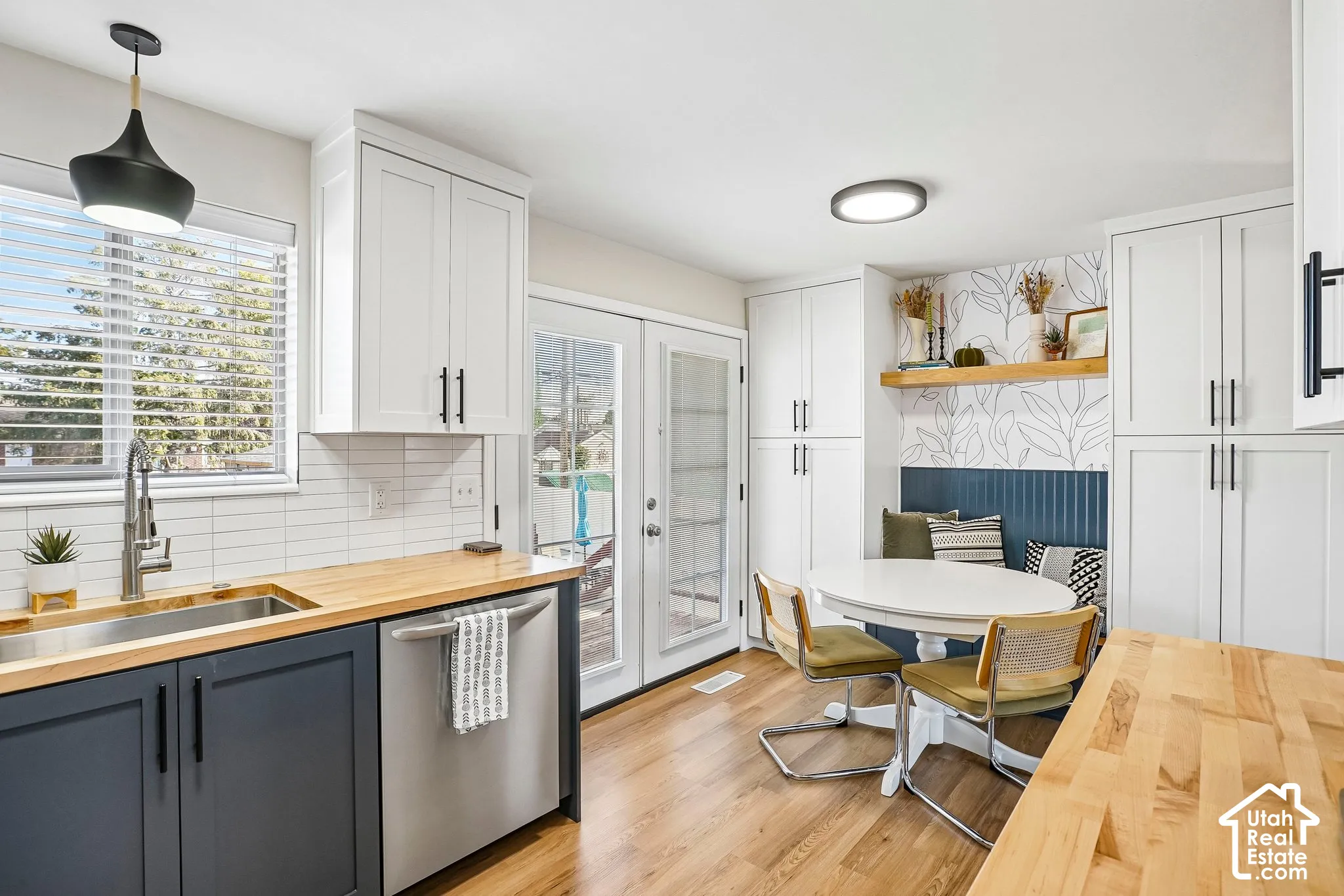 White shaker-style cabinetry, wood-finish countertops, stainless steel sink, tile backsplash, and light wood-finish flooring