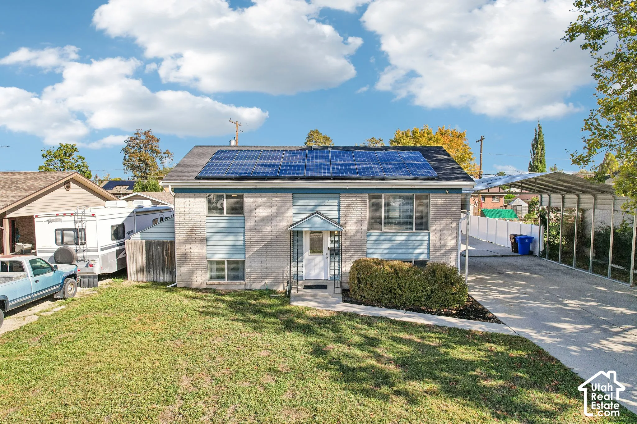 Brick and siding exterior featuring solar panels, a covered entry, and a paved driveway with an attached carport