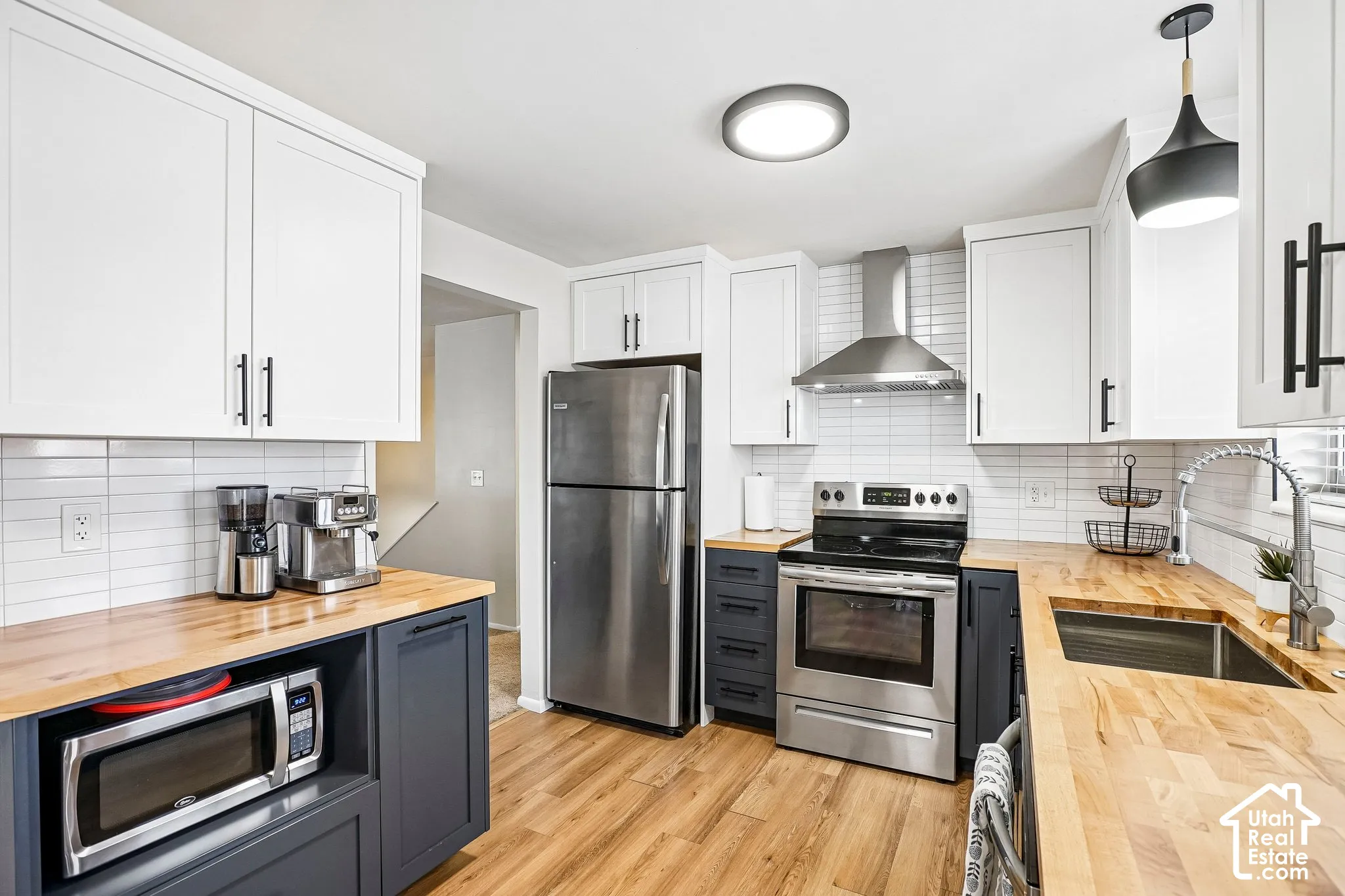 Kitchen featuring wood-finish flooring, two-tone cabinetry, wood countertops, stainless steel appliances, and a tile backsplash