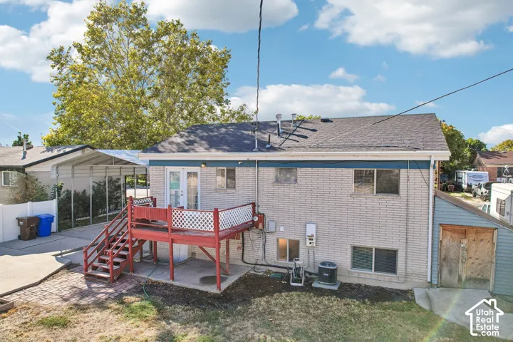 Rear exterior featuring a red-stained wooden deck with white lattice railing, light-colored brick siding, a ground-level patio, and an attached carport