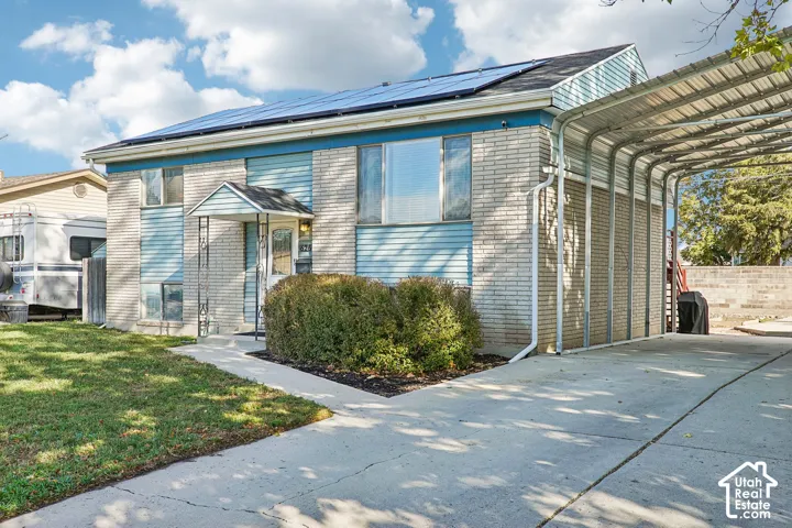 Brick and siding exterior with a covered entry, solar panels, a concrete driveway, and an attached carport