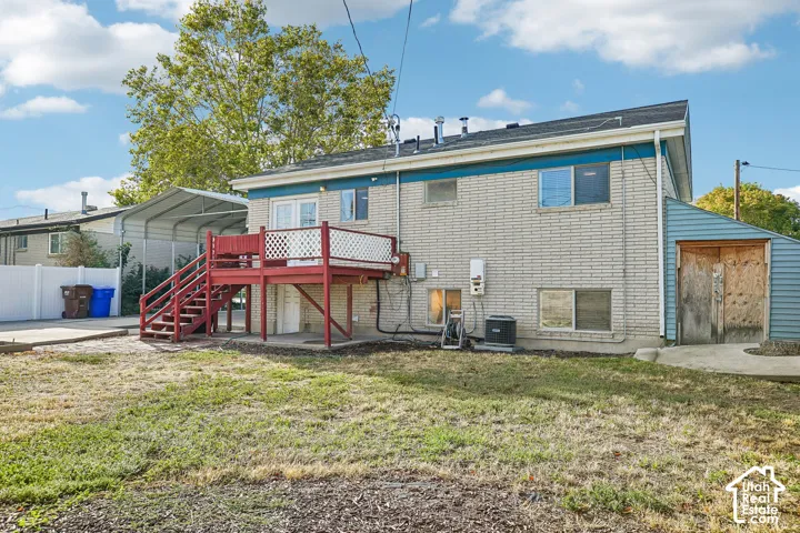 Rear exterior featuring a red deck with lattice railing, light-colored brick siding, a blue-sided attached shed, a white privacy fence, and a metal carport structure