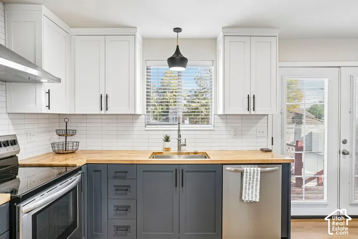 Two-tone cabinetry with white upper cabinets and dark lower cabinets, wood-finish countertops, stainless steel appliances, and a white subway tile backsplash