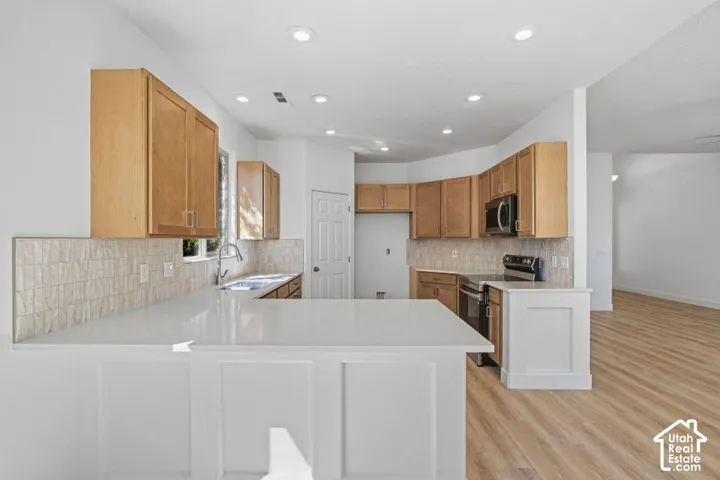 Kitchen featuring light wood-finish cabinetry, white solid surface countertops, and an integrated stainless steel sink