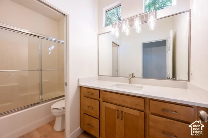 Wood-finish flooring, light wood cabinetry, white countertop, and a built-in tub with a sliding glass door