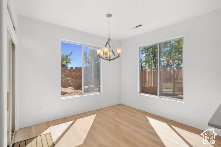 Wood-finish flooring, two large windows, modern chandelier, white walls, and a sliding glass door