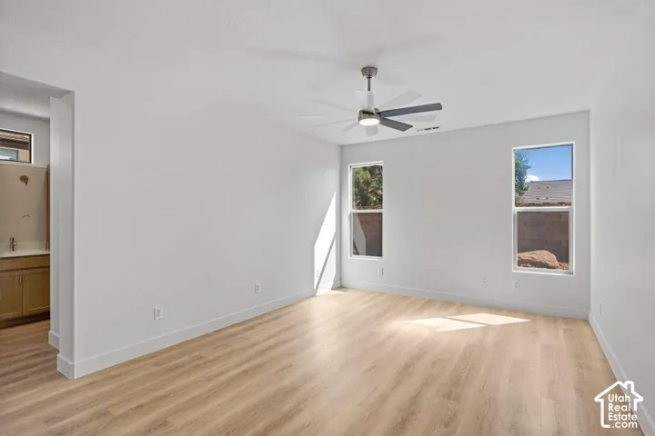 Spacious interior with wood-finish flooring, two large windows, a ceiling fan, and an integrated vanity area with cabinetry and a countertop