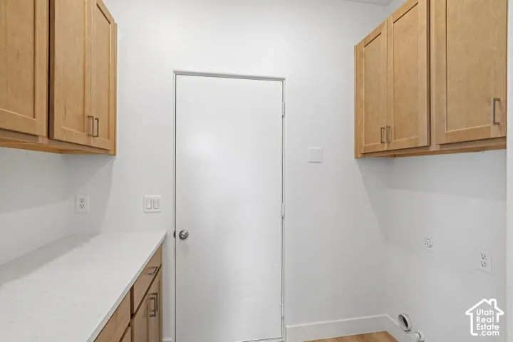 Wood-finish cabinetry with silver-tone hardware, white countertops, and wood-finish flooring