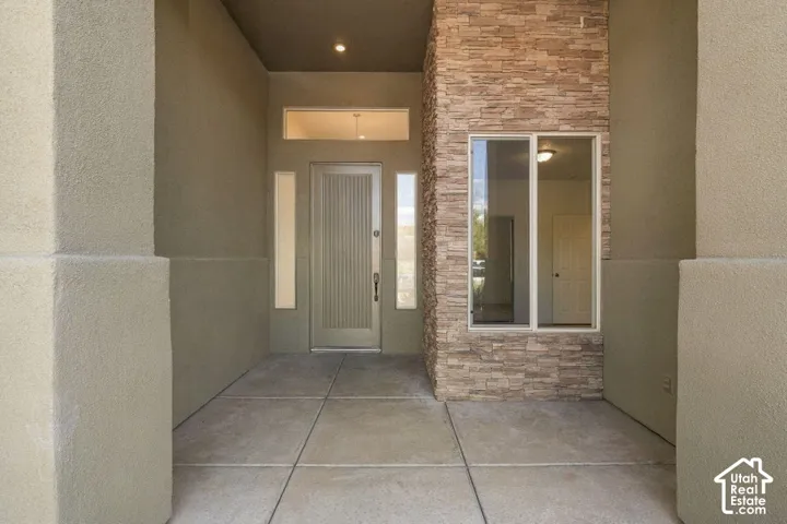 Stucco exterior with stone veneer accents, concrete pathway, recessed lighting, and a front entry door with vertical paneling